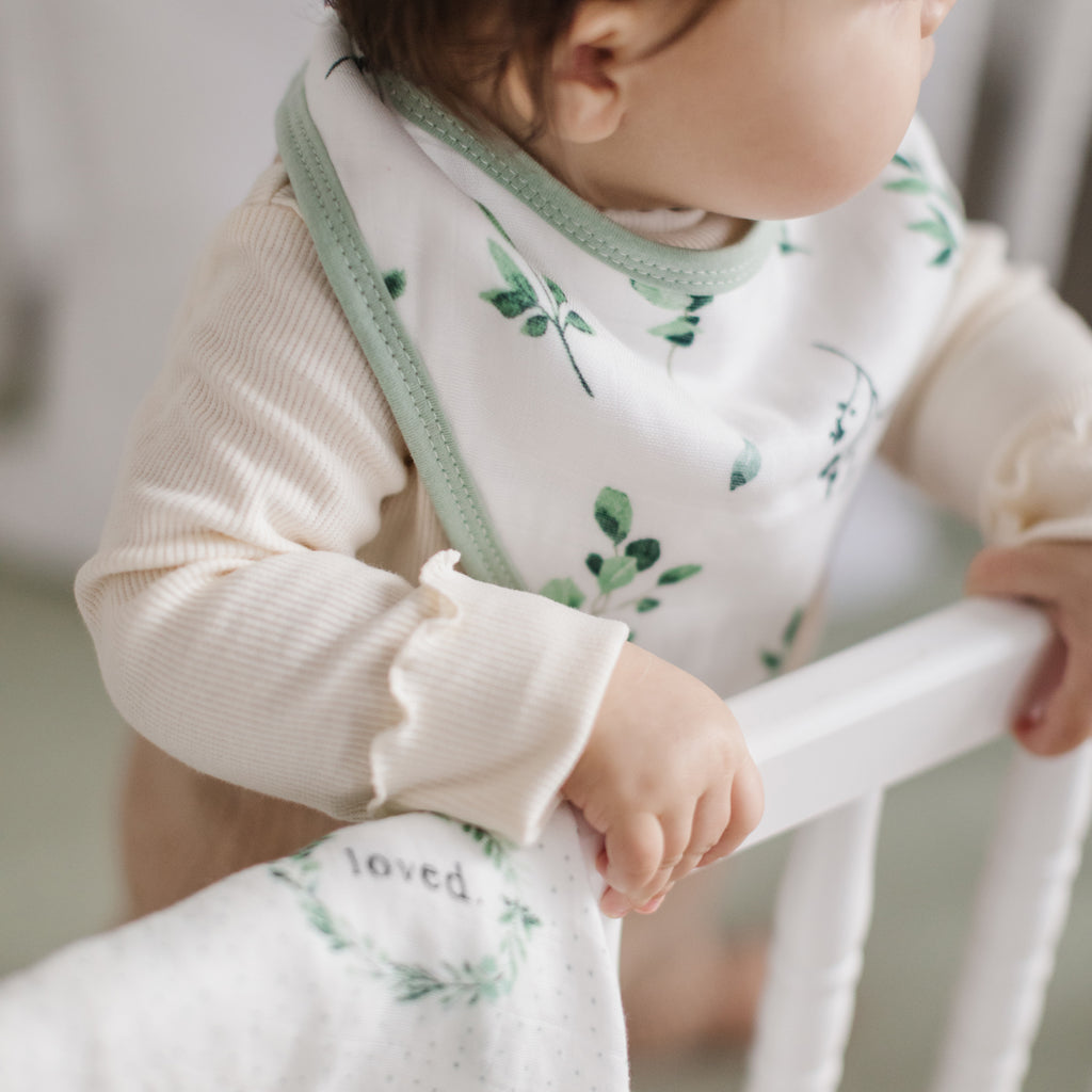 Smiling baby on a city car crib sheet with grey ground and cute cars in pop colours. Baby wears white and ochre stripe bandana bib