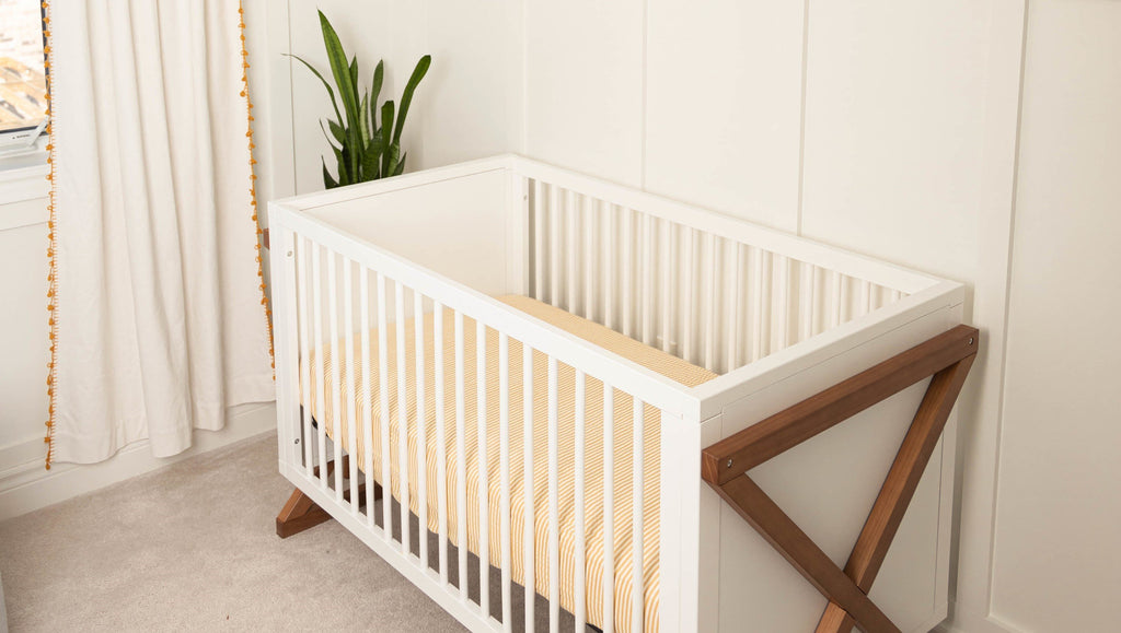 Fun boy or gender neutral nursery features a white and wood crib featuring a bamboo cotton muslin crib sheet in an ochre and white stripe print. Board and battan walls with grey dots and elephant wall head decorate the walls.
