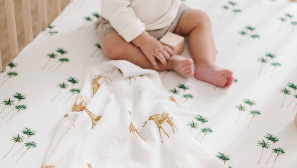 The perfect modern safari nursery. Featuring a dark walnut babyletto Hudson crib paired with black and white tribal pattern crib sheet. A green palm tree with white ground swaddle drapes on the crib. Wall tapestry and potted plant are added for decor
