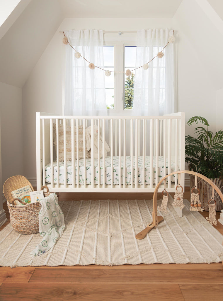Beautiful image of a farmhouse inspired gender neutral nursery. Natural textures in the rug and baskets compliment the pops of green in the watercolour foliage crib sheet printed on a high quality muslin fabric made from cotton and bamboo. 