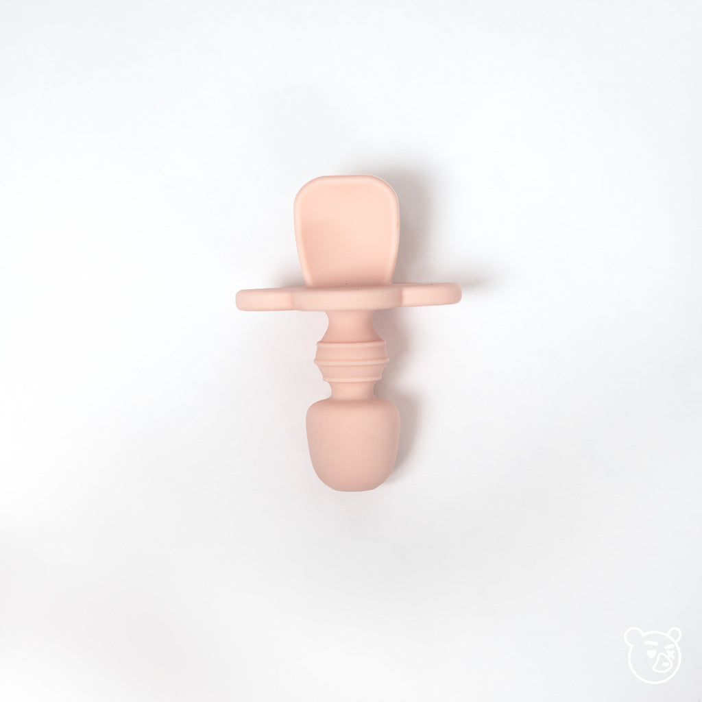 Toddler training spoon in blush pink on white background.
