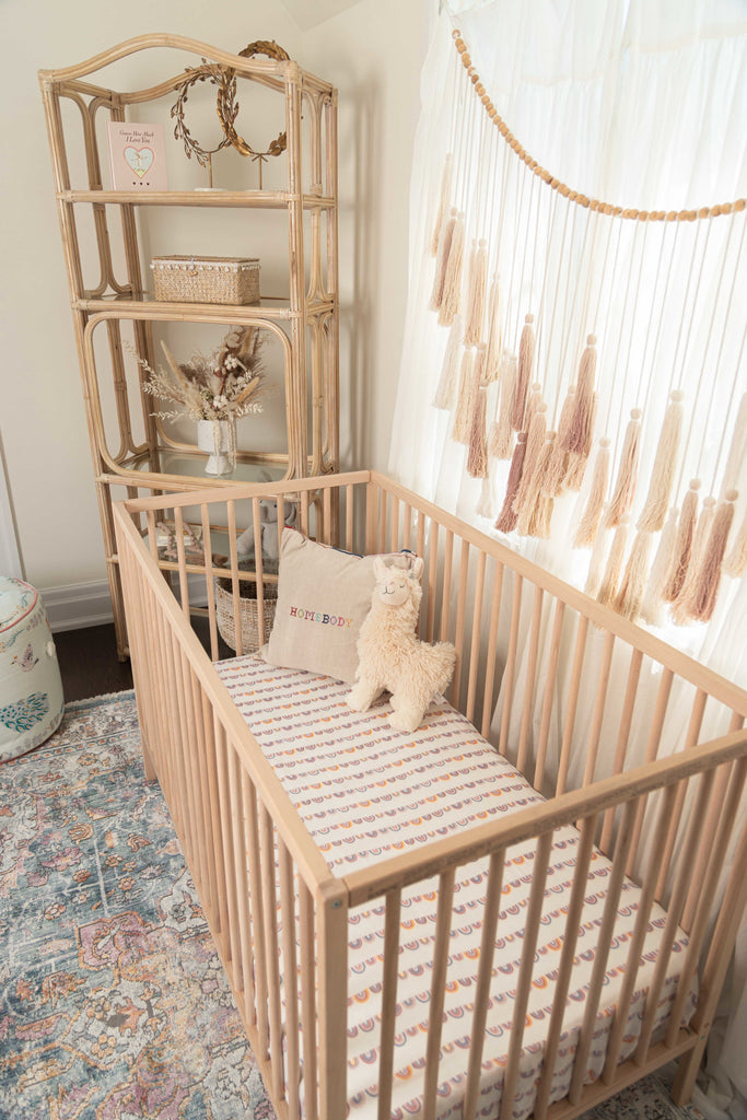 Boho nursery featuring beech word crib and a vintage rattan shelf. Styled with a bright linear rainbow crib sheet to pop in this neutral nursery.
