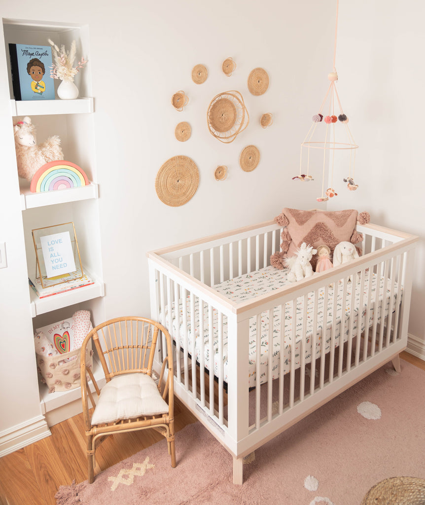 Boho nursery, featuring white and natural crib centres the room with a wildflower printed crib sheet. Hanging natural baskets, rattan chair and butterfly mobile for décor.