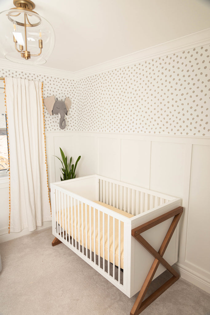  Gender neutral nursery featuring a white and wood crib featuring a bamboo cotton muslin crib sheet in an ochre and white stripe print. 