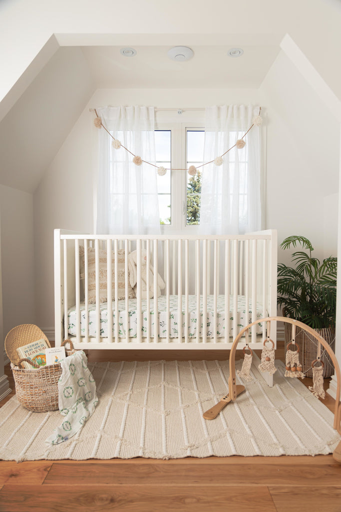 Farmhouse inspired gender neutral nursery. Natural textures in the rug and baskets compliment the pops of green in the watercolour foliage crib sheet printed on a high-quality muslin fabric made from cotton and bamboo.