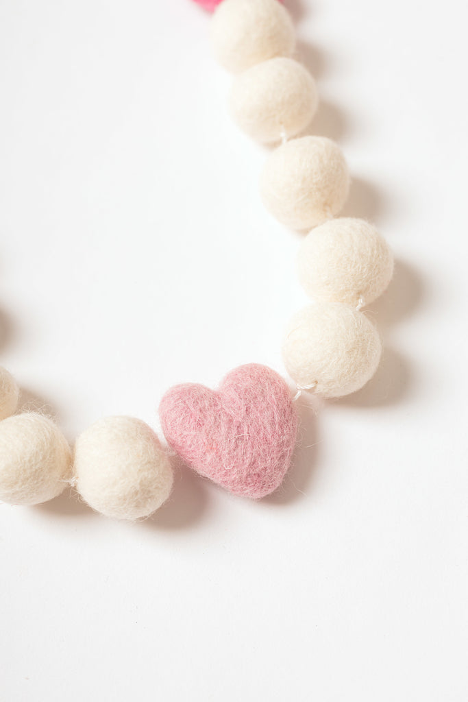 close up image of pink felt heart strung beside white felt balls