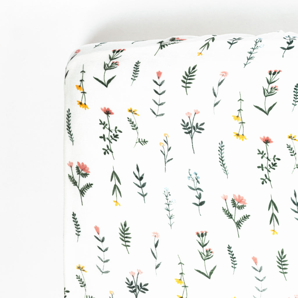 Photo of corner of a crib mattress with boho wildflower print. florals are blush, yellow, and periwinkle with soft green stems and leaves