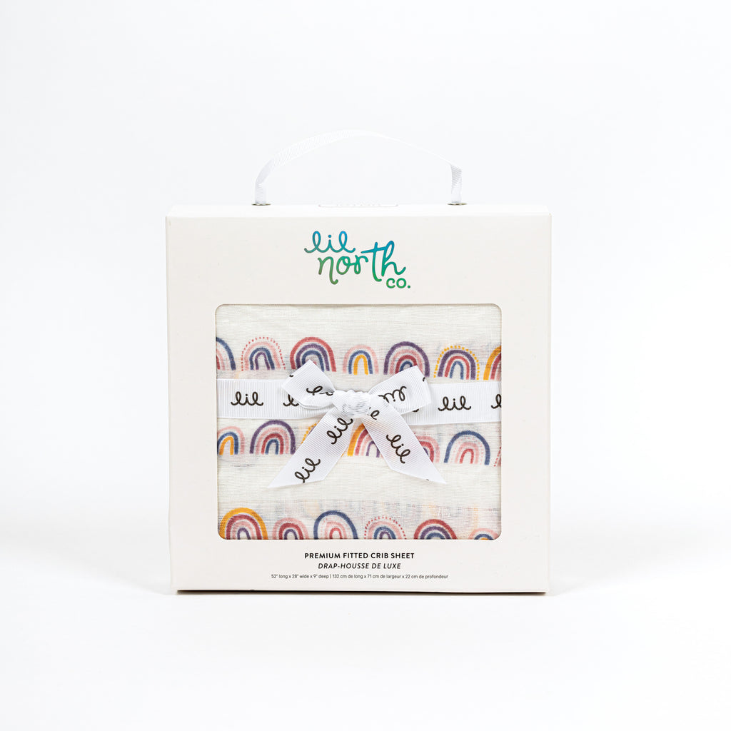 Perfectly boxed baby gift featuring linear rainbow crib sheet with yellow periwinkle blush and mauve arches