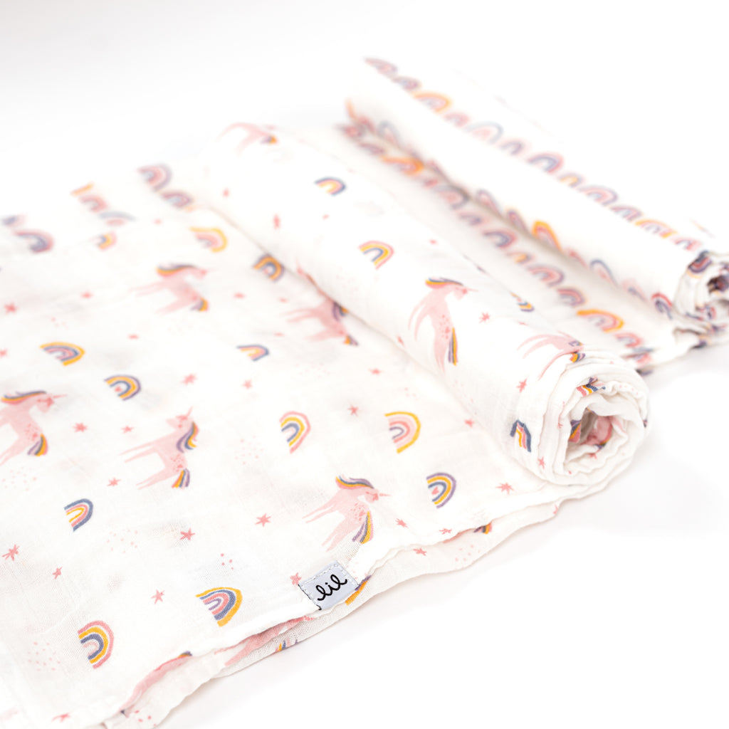 swaddle blankets rolled one print is linear rainbows and the other is tossed unicorn and rainbows in blush periwinkle yellow and mauve