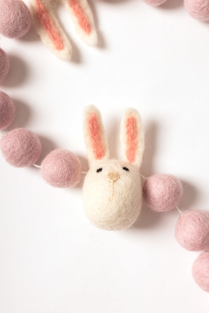 close up image of a felt bunny head on the garland beside blush coloured felt balls