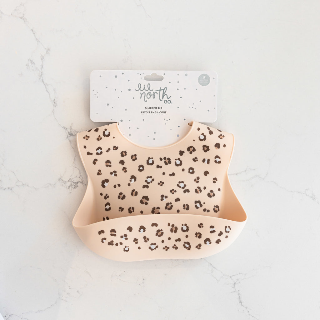 Silicone bib in sand colour with cheetah spots in brown and taupe on white counter.