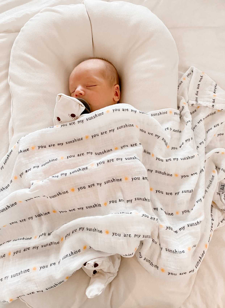 Image courtesy of @ginaraebarclay - little baby boy sleeps on a baby lounger while covered in a you are my sunshine muslin swaddle