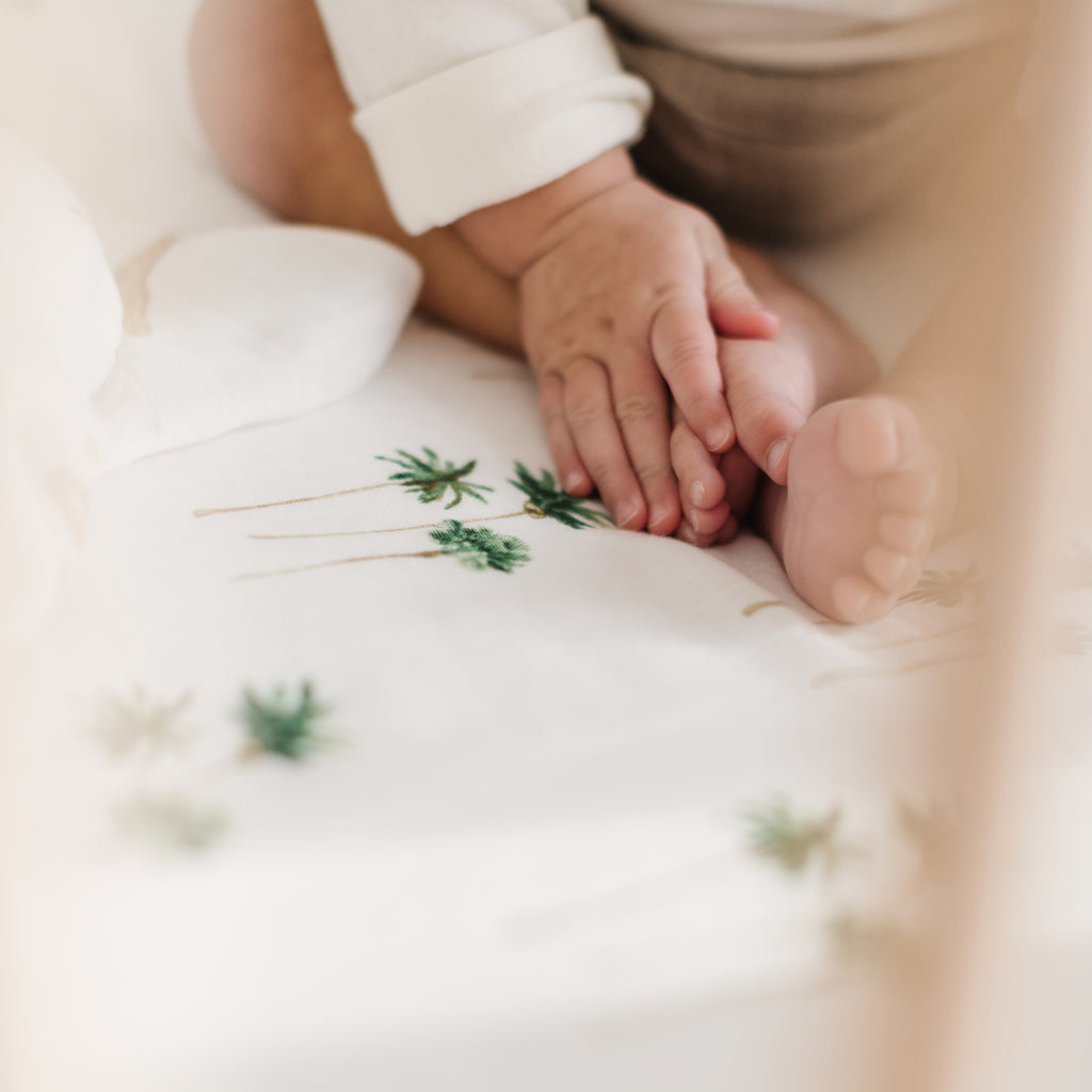 close up image of little hands and baby feet on a palm tree printed crib sheet