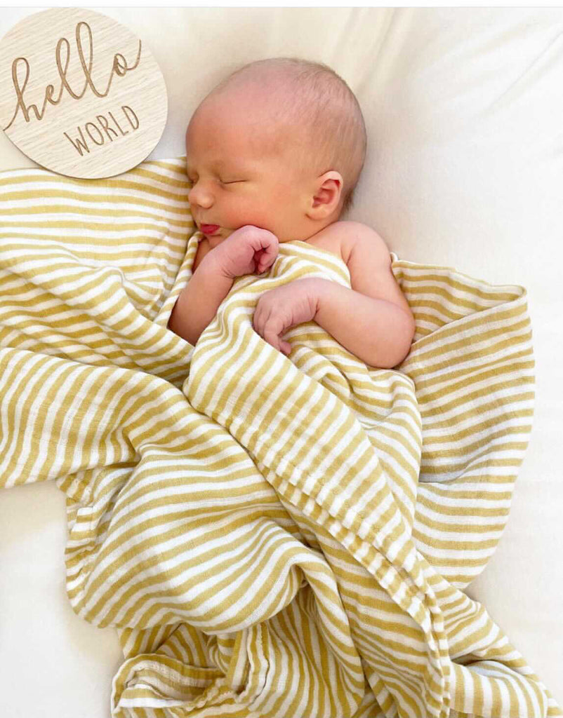 Image of newborn baby swaddled in a yellow ochre stripe muslin swaddle