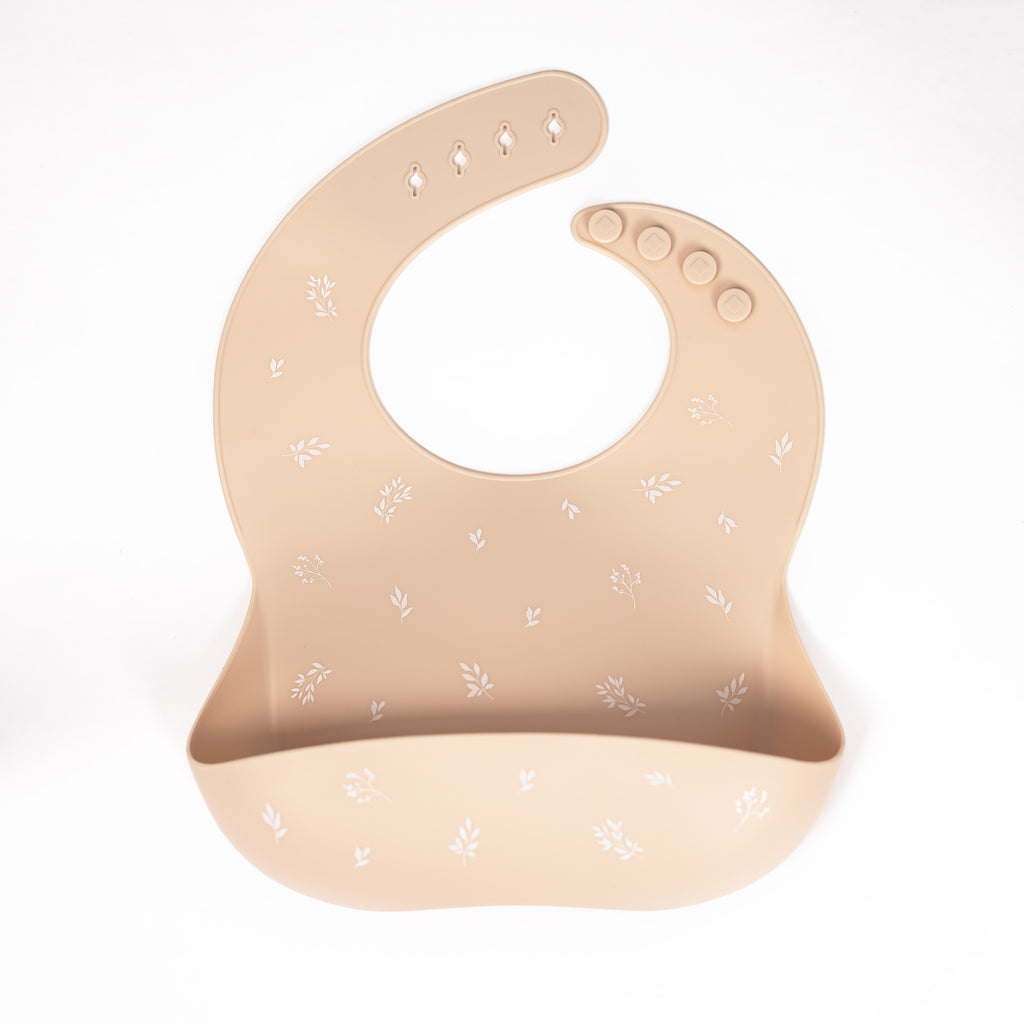 Safety tested silicone bib in shifting sand colour with white foliage print.