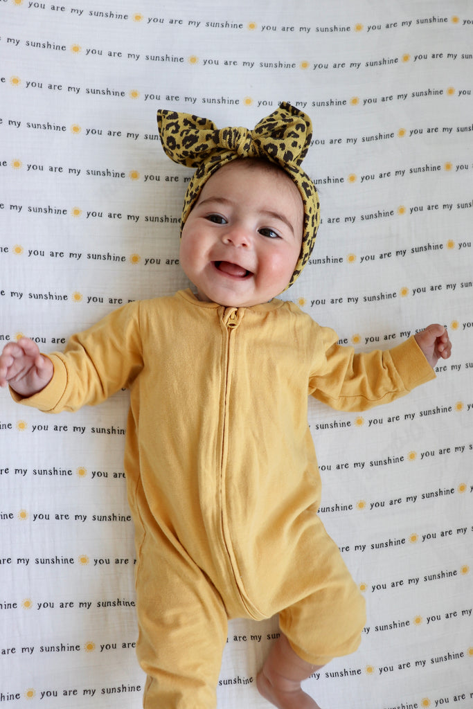 smiling little girl in yellow onesie lies on a you ar emy sunshine typography crib sheet