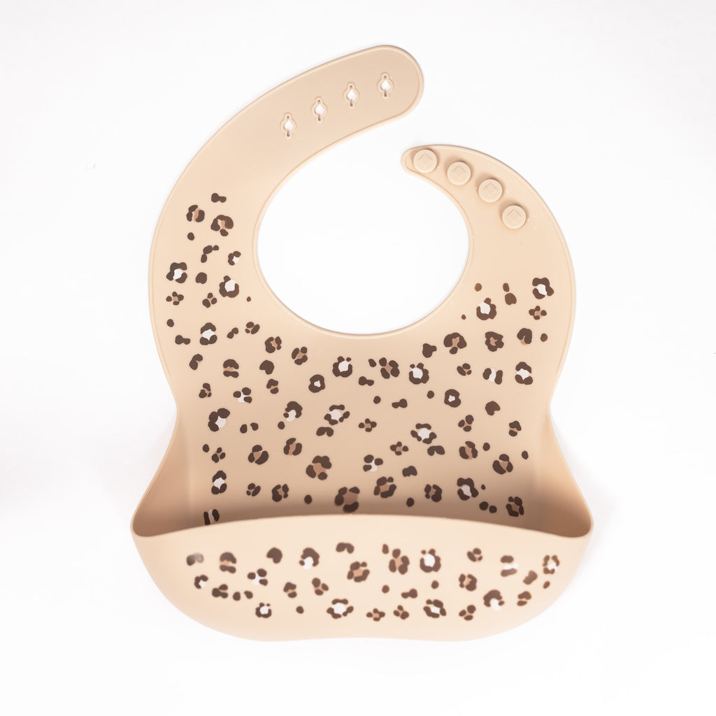 Silicone bib in sand colour with cheetah spots in brown and taupe on white background.