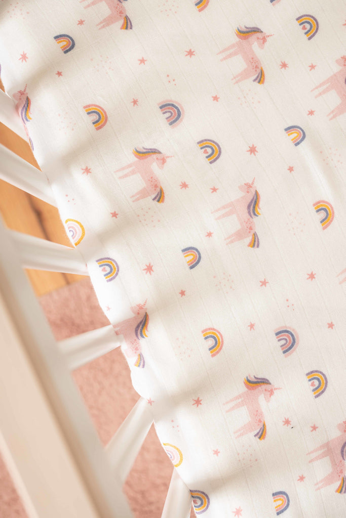 Lifestyle image of Unicorn and rainbow tossed print in white babyletto crib