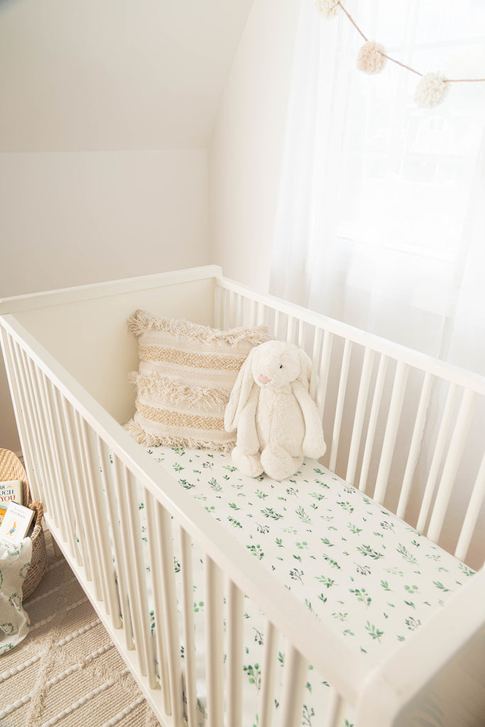 Lifestyle image of modern farmhouse nursery. White crib features watercolour foliage crib sheet, ivory pillow and large jellycat bunny