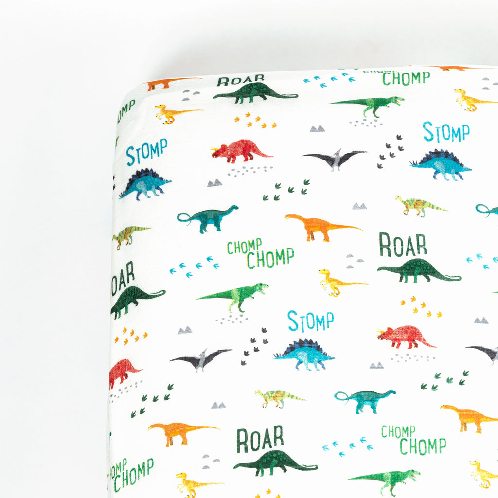 Corner image of premium bamboo cotton muslin crib sheet. Print features various bright dinos with sayings like roar and stomp