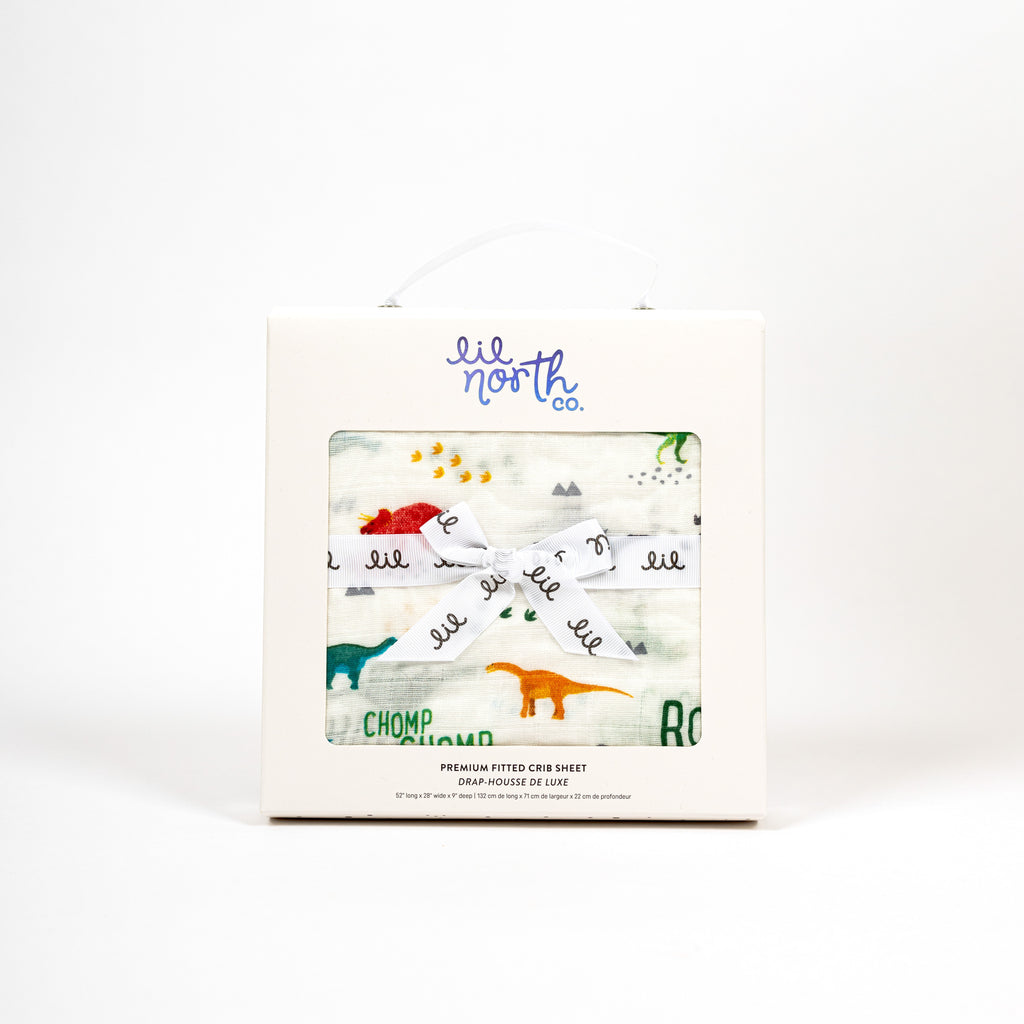 Perfectly packaged dino muslin crib sheet in white box with lil north co logo and ribbon tied in a bow