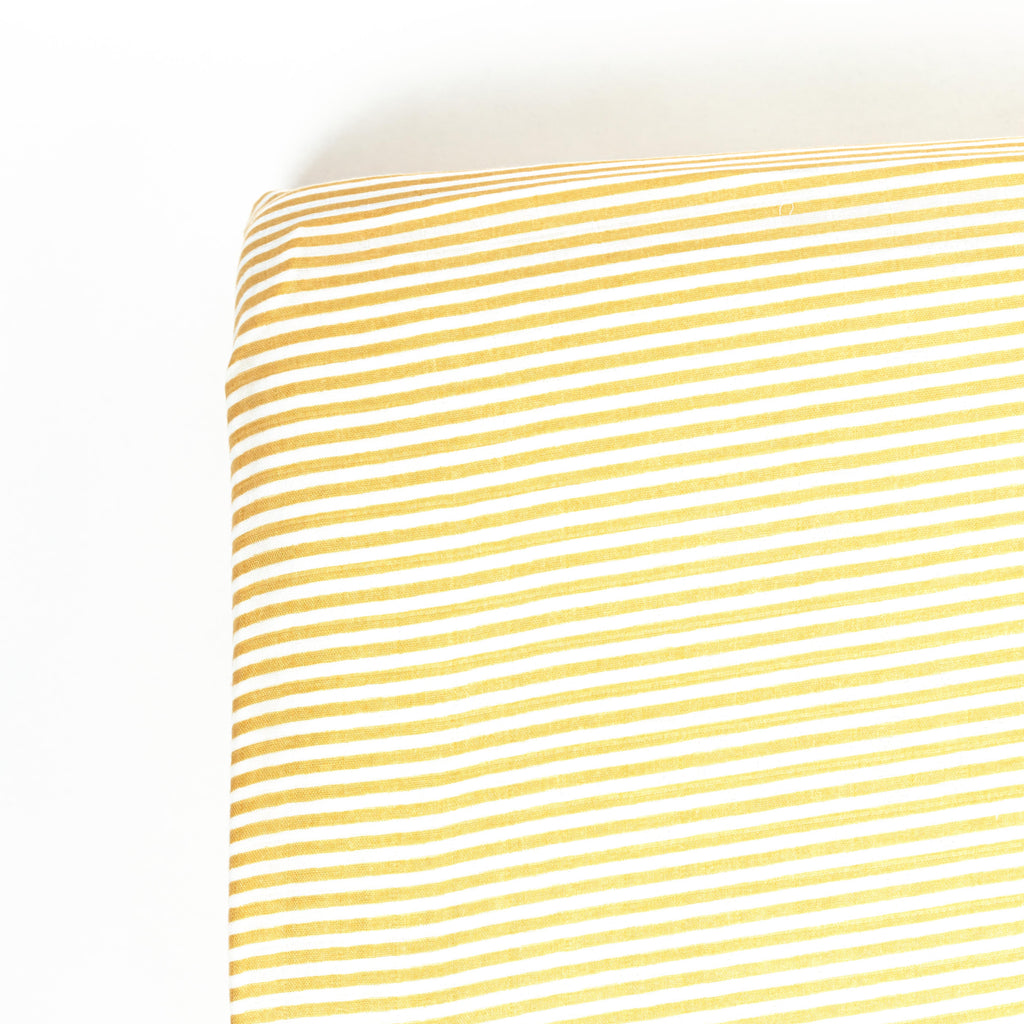 Corner image of premium bamboo cotton muslin crib sheet in ochre and white stripe