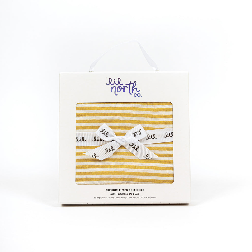 Ochre stripe muslin crib sheet in white box with holographic lil north co label and white ribbon tied in a bow