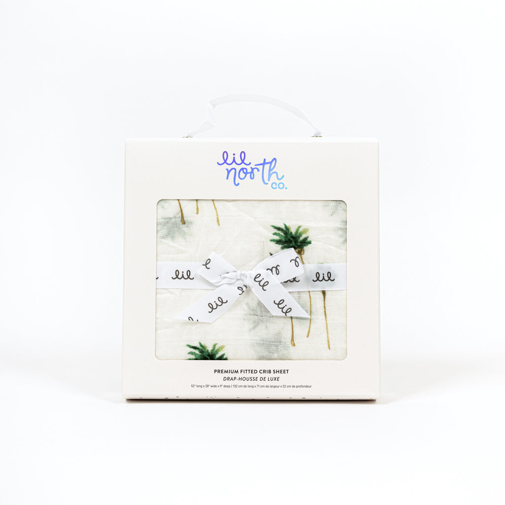 perfectly packaged crib sheet features palm tree print on premium bamboo cotton muslin. White box with holographic logo and ribbon tied in a bow makes this the perfect baby shower gift
