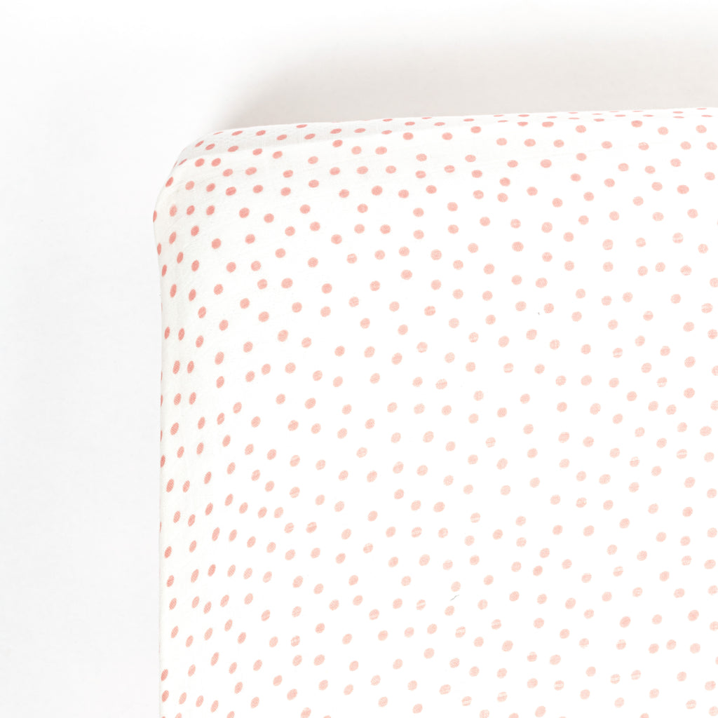 Photo of the corner of a crib mattress with a blush dot muslin crib sheet
