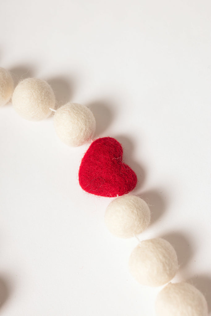 close up image of red felt heart strung beside white felt balls