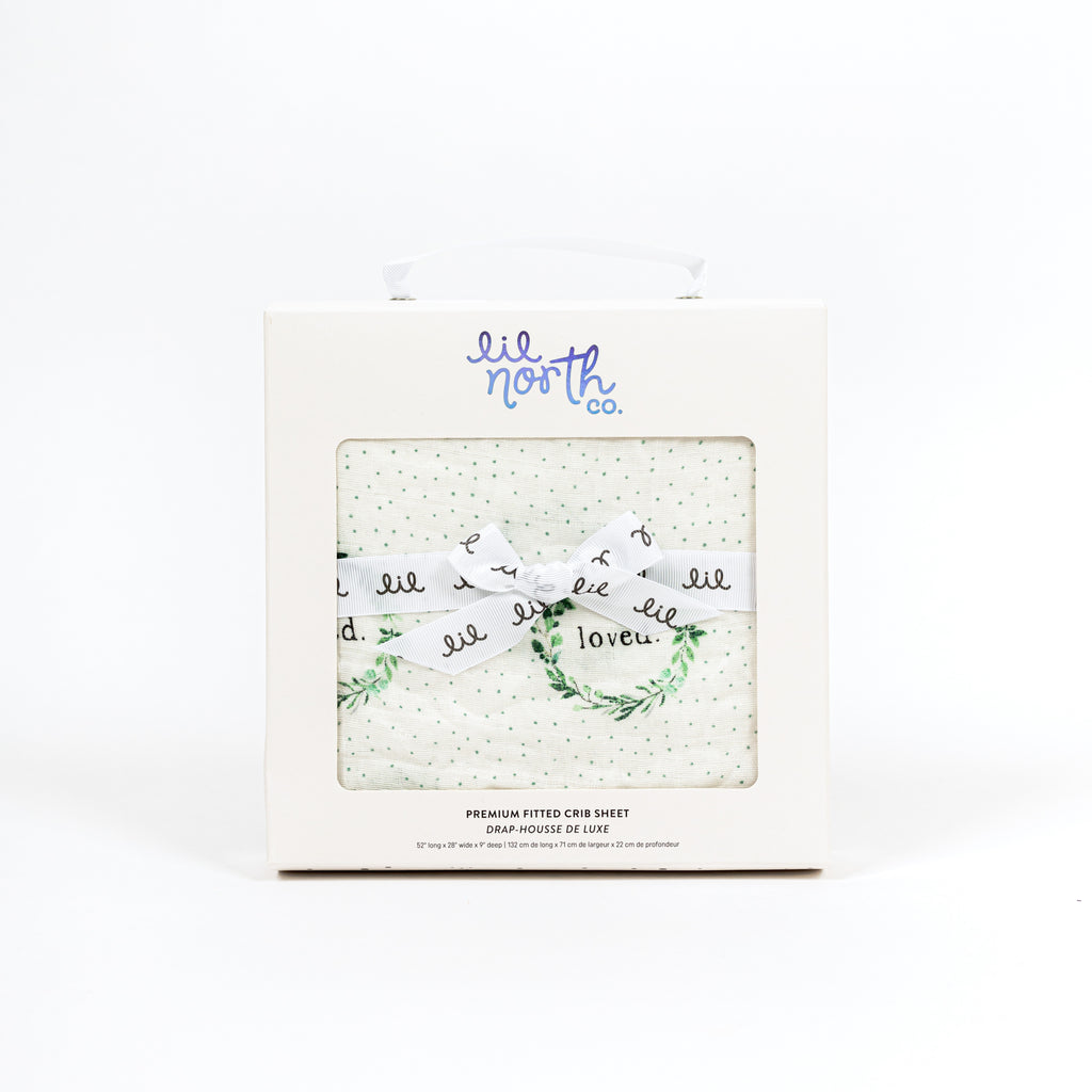 Beautiful white box with lil north co label and white ribbon tied in a bow featured sage and green watercolour foliage wreath with loved in the middle and sage dots tossed in the background of this muslin crib sheet