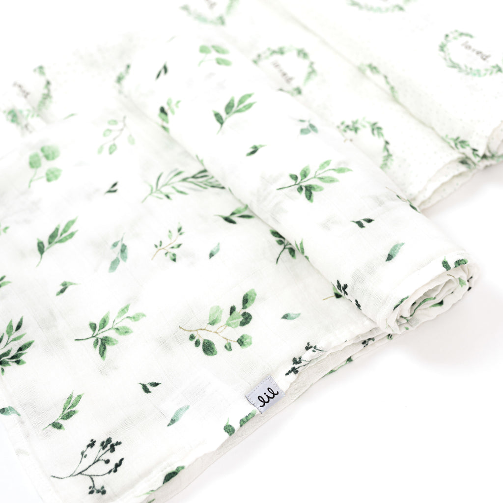 rolled swaddles featuring one green foliage and leaves swaddle and one foliage wreath with loved saying in the middle of the wreath