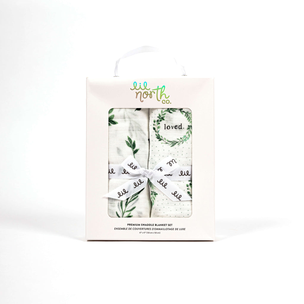 beautiful boxed baby gift featuring two premium swaddles, one watercolour foliage and one foliage wreath with loved saying in each wreath