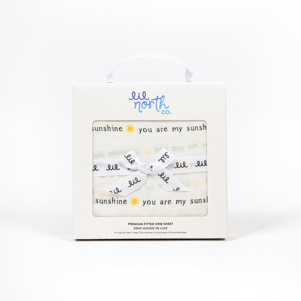 White box with lil north co logo and ribbon tied in a bow. Features you are my sunshine muslin crib sheet in black text with yellow sun