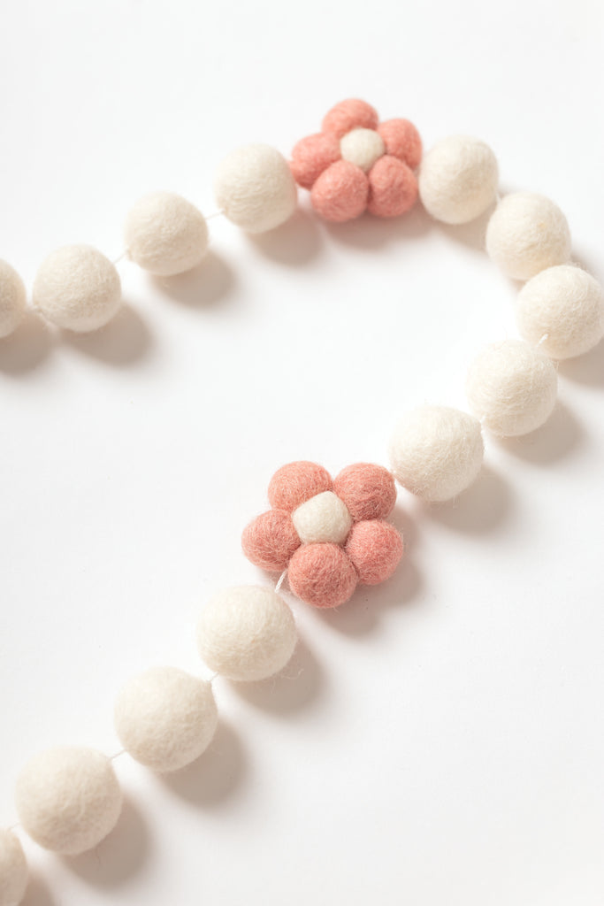 close up image of daisy garland. The daisy has blush petals and white centre and is strung with white felt balls