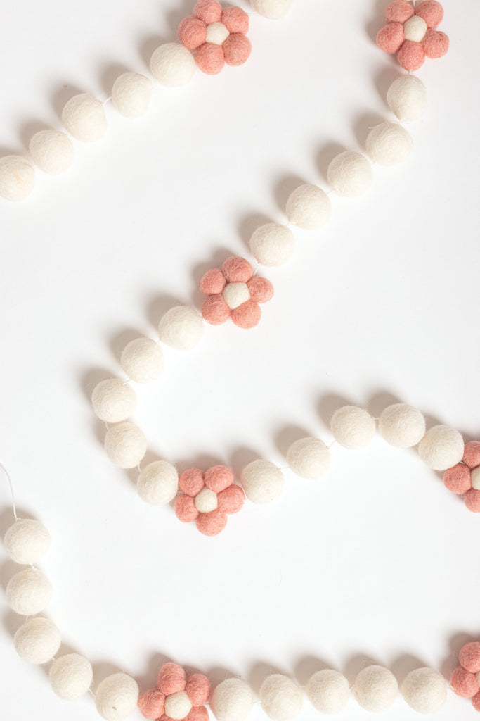 image of a daisy garland. the garland has little felt flowers with blush petals and white centre strung between white felt balls