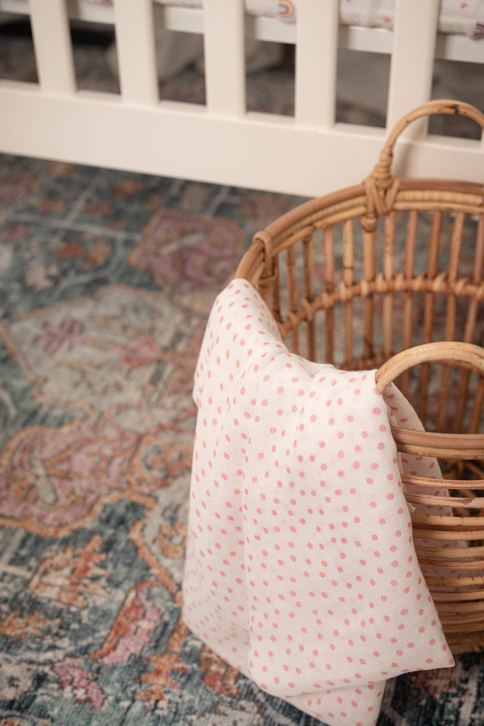 image of a blush dot swaddle hanging from a rattan storage basket