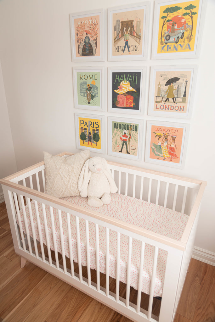 lifestyle image of a nursery. The nursery has a white crib with a blush dot crib sheet. Above the crib is a gallery wall of images from around the globe