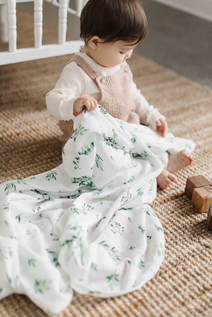Image of little girl holding a watercolour foliage patterned muslin swaddle