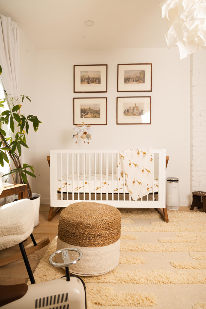 image of @jaclyngenovese nursery. Nursery is all neutral toned with natural textures and features a white crib with a watercolour giraffe printed swaddle and crib sheet from lil north co